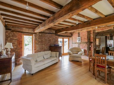 A living room with a striped sofa an armchair wooden dining table and exposed beams at Munderfield Mill in Munderfield near Bishops Frome