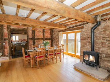 A dining room with a wooden table and six chairs near a wood burning stove at Munderfield Mill in Munderfield near Bishops Frome