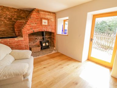 A room with a white sofa a brick fireplace with a wood stove a wicker basket wooden flooring and a glass door at Munderfield Mill in Munderfield near Bishops Frome