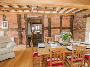 A dining room with a wooden table set with plates and glasses and a vase of flowers next to a beige armchair at Munderfield Mill in Munderfield near Bishops Frome