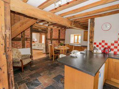 A kitchen with wooden beams and a tiled floor next to a dining area with a round table and chairs at Munderfield Mill in Munderfield near Bishop's Frome