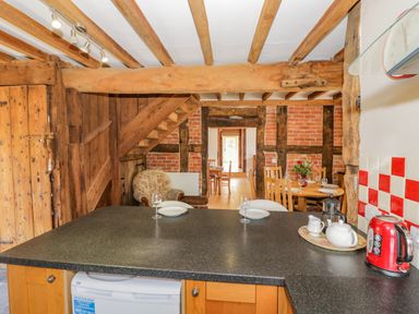 A kitchen with wooden beams and a black countertop overlooking a dining area with wooden chairs and a floral armchair at Munderfield Mill Munderfield near Bishops Frome