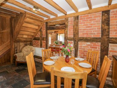 A dining room with a round wooden table set with plates and glasses surrounded by wooden chairs and exposed wooden beams on brick walls at Munderfield Mill in Munderfield near Bishops Frome