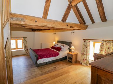 A bedroom with a double bed bedside tables wooden beams and floral curtains at Munderfield Mill in Munderfield near Bishops Frome