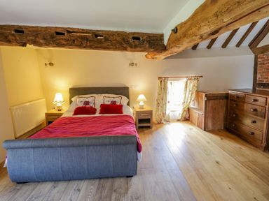 A bedroom with a double bed two bedside tables with lamps wooden chest of drawers and a small window with floral curtains at Munderfield Mill in Munderfield near Bishops Frome