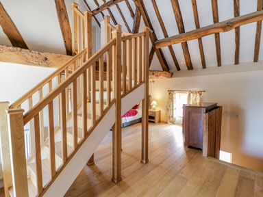 An upstairs room with wooden stairs exposed ceiling beams a chest of drawers a window with floral curtains and a bedside table with a lamp at Munderfield Mill in Munderfield near Bishops Frome