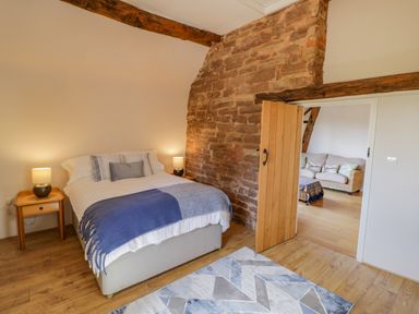 A bedroom with a double bed bedside tables lamps and an open door showing a sitting area at Munderfield Mill in Munderfield near Bishops Frome
