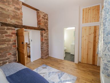 A bedroom with wooden floor exposed brick wall wooden doors and a bathroom at Munderfield Mill in Munderfield near Bishops Frome