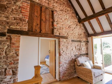 A room with exposed stone walls wooden beams a wicker armchair and an open door leading outside at Munderfield Mill in Munderfield near Bishops Frome