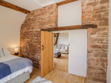 A bedroom with a bed side table lamp a wooden door and an exposed stone wall at Munderfield Mill in Munderfield near Bishops Frome
