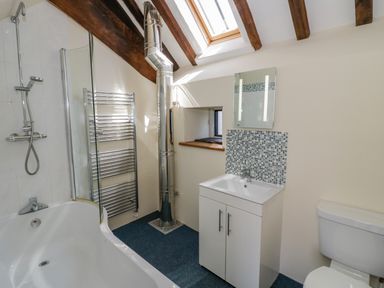 A bathroom with a bathtub shower combo sink cabinet toilet and exposed wooden beams at Munderfield Mill in Munderfield near Bishops Frome