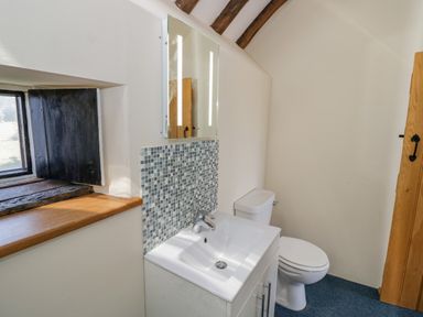 A bathroom with a sink under a mirror a toilet and a small window at Munderfield Mill in Munderfield near Bishops Frome