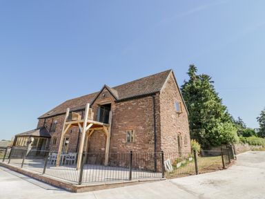An exterior view of a brick building with a wooden balcony and metal railings at Munderfield Mill in Munderfield near Bishops Frome