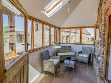 A small enclosed sunroom with wicker furniture and glass windows at Munderfield Mill in Munderfield near Bishop's Frome