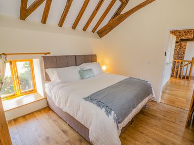 A bedroom with a large bed wooden beams on the ceiling and a small window at Munderfield Mill in Munderfield near Bishops Frome