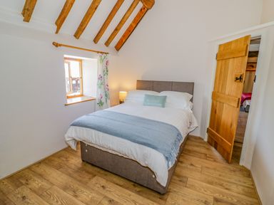 A bedroom with a double bed next to a window with floral curtains and a wooden door at Munderfield Mill in Munderfield near Bishops Frome