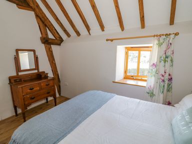 A bedroom with wooden beams a wooden dresser with mirror a bed near a window with floral curtains at Munderfield Mill Munderfield near Bishops Frome