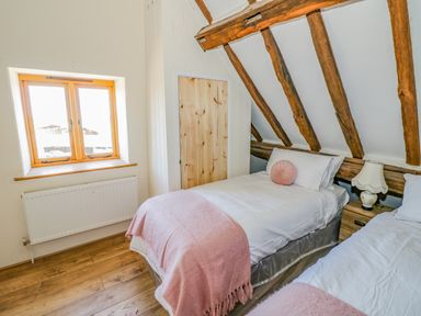 A bedroom with two single beds a window a wooden door exposed wooden beams and a bedside table with a lamp at Munderfield Mill in Munderfield near Bishops Frome