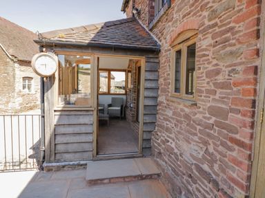 An entrance to a stone and wood building with a clock on the exterior wall at Munderfield Mill in Munderfield near Bishops Frome