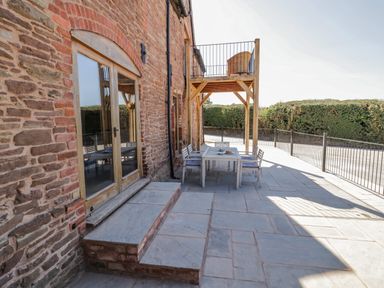 An outdoor patio with a stone floor and wooden table with chairs next to a brick building at Munderfield Mill in Munderfield near Bishops Frome