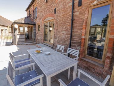 An outdoor patio area with a wooden table and chairs set next to a stone building at Munderfield Mill in Munderfield near Bishops Frome