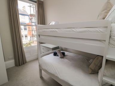 A bedroom with a white bunk bed next to a window with beige curtains at Spinnaker House in Scarborough