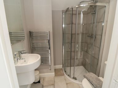 A bathroom with a sink a towel radiator a curved glass shower enclosure and a toilet with a rug on it at Spinnaker House in Scarborough