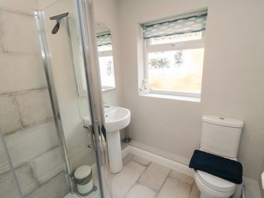A bathroom with a shower, sink, toilet, and a window with a blind at Spinnaker House in Scarborough