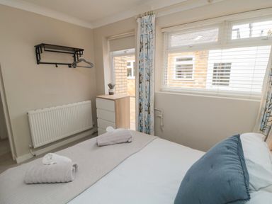 A bedroom with a bed with folded towels on it a chest of drawers a window with blinds and curtains at Spinnaker House in Scarborough