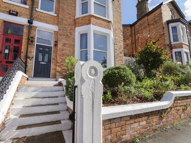 A front entrance with white steps black handrail and greenery next to a brick house at Spinnaker House Scarborough