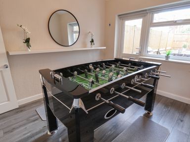 A room with a foosball table a round mirror on the wall and a window showing a fenced outdoor area at Spinnaker House in Scarborough