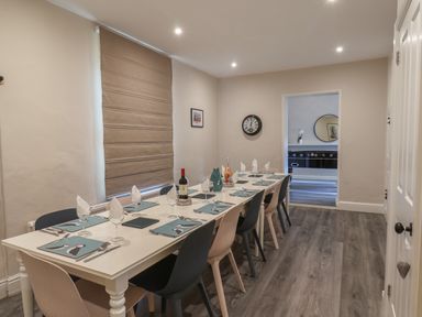 A dining room with a long white table set with placemats cutlery wine glasses and bottles with mixed color chairs at Spinnaker House in Scarborough