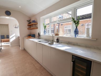 A kitchen with a long countertop a sink knives on a block shelves with glasses and decorations at Spinnaker House in Scarborough