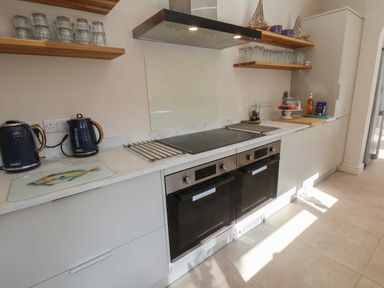 A kitchen with two ovens a stovetop blue kettle and teapot open shelves with glasses at Spinnaker House in Scarborough