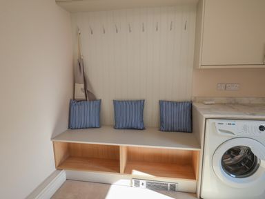 A laundry room with a bench with three blue pillows and hooks on the wall above at Spinnaker House in Scarborough