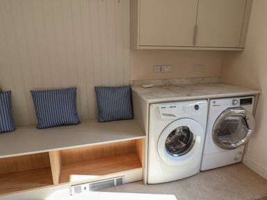 A laundry room with a washing machine and dryer under a countertop with storage cabinets and a bench with blue striped cushions at Spinnaker House in Scarborough