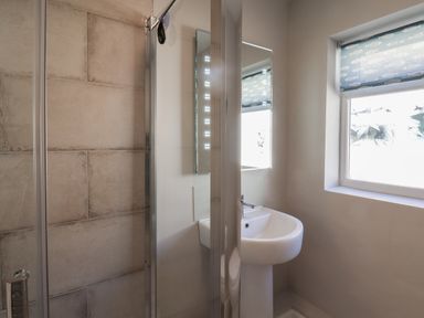 A bathroom with a shower enclosure a pedestal sink a mirror and a window with a patterned blind at Spinnaker House in Scarborough