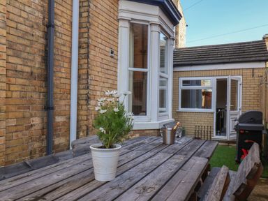 An outdoor patio area with a wooden table and benches a potted plant on the table a bucket with a bottle and glasses next to a brick house at Spinnaker House in Scarborough