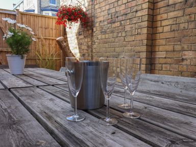A wooden outdoor table with a metal ice bucket containing a champagne bottle and three champagne flutes on the table at Spinnaker House in Scarborough