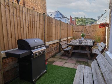 An outdoor patio area with a barbecue grill wooden benches and a wooden dining table with chairs at Spinnaker House in Scarborough