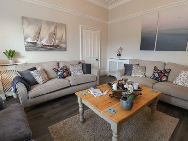 A living room with two beige sofas a wooden coffee table with cups and a plant and wall art at Spinnaker House in Scarborough