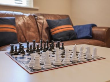 A chessboard with chess pieces set up on a table in front of a brown leather sofa with cushions at Spinnaker House in Scarborough