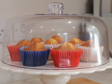 Muffins in colored paper cups on a cake stand with a glass cover in a kitchen