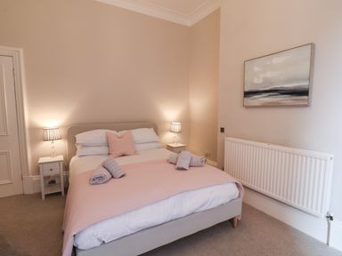 A bedroom with a bed with pink and white bedding two bedside tables with lamps and a painting on the wall at Spinnaker House in Scarborough