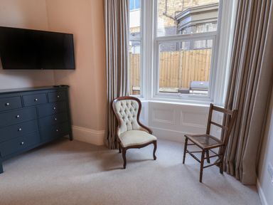 A room with a wall-mounted television a dresser and two chairs by a window at Spinnaker House in Scarborough