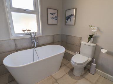 A bathroom with a freestanding bathtub a toilet and framed whale pictures on the wall at Spinnaker House in Scarborough
