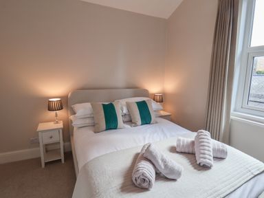 A bedroom with a bed with pillows and rolled towels beside two bedside tables with lamps at Spinnaker House in Scarborough