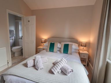A bedroom with a double bed towels on the bed bedside tables with lamps an open door to a bathroom at Spinnaker House in Scarborough