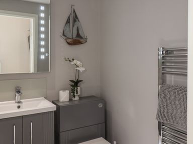 A bathroom with a sink cabinet a mirror a toilet with a shelf above and a towel on a chrome rack at Spinnaker House in Scarborough
