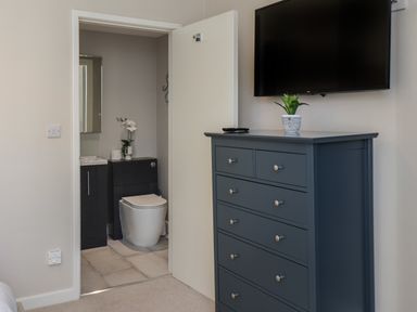 A room with a dark blue chest of drawers and a wall-mounted television next to a door leading to a bathroom with a toilet and a sink at Spinnaker House in Scarborough